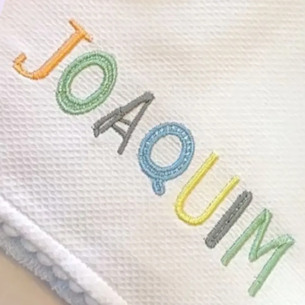 Toalha branca com capuz e o nome Joaquim bordado em letras coloridas